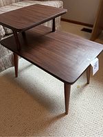Side view of the vintage MCM two-tiered wooden side table showing tapered legs and minor scratches.