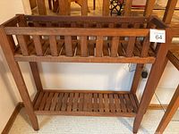 Full view of two tiered wooden plant stand showing the overall structure, slatted shelves, railing on upper tier, and four legs.
