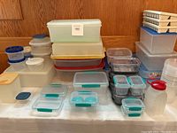 Wide view of multiple stacks of plastic food storage containers including Sistema brand with blue-green snap-lock lids and other assorted containers in various sizes.