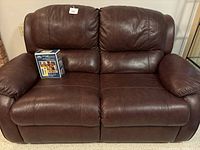 Front view of brown leather reclining loveseat with a boxed leather furniture care package placed on the seat.