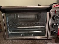 Front view of Black+Decker Crisp 'n Bake air fryer toaster oven showing control knobs and glass door with visible interior racks and tray.