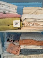 Side view of stacked bath and hand towels in various colors including white, cream, pink, green, and peach showing folded condition and shelf storage.