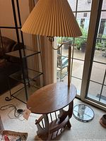 Full view of the vintage floor lamp with wooden oval end table surface and magazine rack base, showing brass stem and beige pleated lampshade.