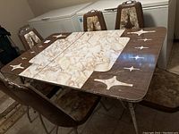 Full view of vintage dining table with six brown vinyl chairs, table has marbled laminate top with geometric inlay and chrome legs