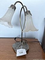 Vintage metal lily pad table lamp with two white glass lily flower-shaped shades and bronze-toned base on a wooden surface.