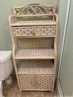 Front view of the cream and blue woven wicker stand showing drawer, shelves, and bottom cabinet