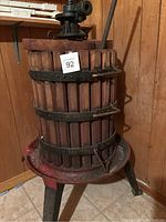 Full view of vintage wooden and metal wine press on metal legs with a crank handle.