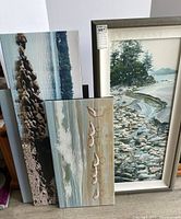 Three canvas pieces leaning against wall: one framed and two unframed.