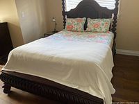Fully assembled wood bedframe with floral bedding and white cover on mattress showing the finished bed setup.