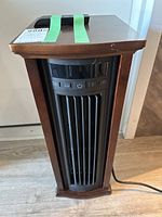 Front view of the electric heater showing wood finish and vertical grille with control buttons at the top.
