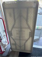 Folding table standing upright showing textured underside and foldable leg outlines