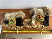 Pair of indigenous style leather moccasins showing side and top, displaying beadwork floral patterns, fur ankle trim, and fringe detail.