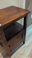 Close-up view of the wooden side table showing the top surface, side panels, and open shelf area.
