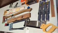 Assortment of hand tools including two saws, an axe, a wooden spirit level, and a long metal ruler.