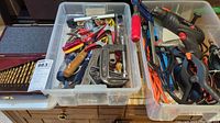 Overview of tools in plastic bins showing drills, clamps, drill bits