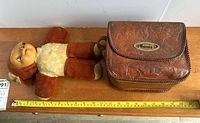 Photo showing the vintage doll lying next to the leather purse with a measuring tape for size reference.