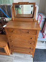 Front view of vintage wooden dresser with attached rectangular mirror and five drawers with wooden knobs.