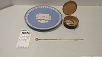 Full view of Wedgwood blue Jasperware plate next to vintage watch in leather case and gold-tone locket necklace.