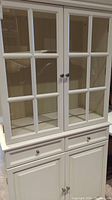 Full front view of white buffet hutch showing upper glass doors and lower cabinets