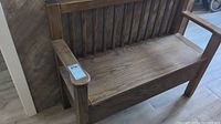 Front view of oak storage bench against wall showing slatted back, arms and seat closed.