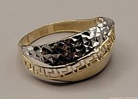 Oblique view of two-tone gold ring showing detailed textured white gold section and smooth yellow gold Greek key pattern band.