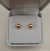 Front view of two small round polished gold stud earrings set on a light grey velvet cushion inside an open box.