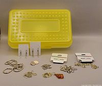 Overview of all jewellery pieces laid out with yellow storage box in background, showing chains, earrings, pendant, and cufflink.
