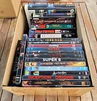 Top view of box containing 13 DVD and 8 VHS movies in good used condition.