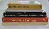 Five art books stacked showing titles on spines: The Fine Arts in Canada, Edmund Morris - Frontier Artist, Landmarks of Canadian Art, Victorian Painters, The Works of Joseph Legare.