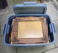 Open Rubbermaid tote showing the wooden picture frame with decorative corners on top