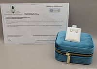 Photo of earrings on white display card with appraisal certificate and teal velvet zippered box behind them, showing packaging and appraisal.