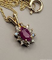 Close view of oval ruby and diamond halo pendant alongside lobster clasp marked 10KT