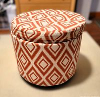 Round storage ottoman showing side view with patterned orange and white fabric upholstery.