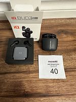 Photo showing the iQ Budz Mirco earbuds inside the charging case beside the original box and packaging insert on a wooden surface.