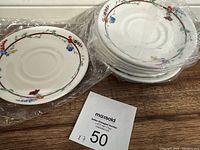 Seven Royal Doulton bone china saucers with floral patterns stacked and wrapped in plastic.