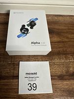 Photo of the white rectangular box with Vankyo Alpha X180 earbuds image and branding on front, placed on wooden surface with MaxSold auction card nearby.