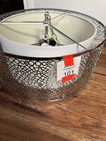 Close-up of the metal outer frame composed of overlapping circular cutouts in a shiny silver finish around the drum shade.