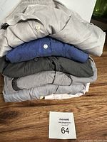 Stack of five men's dress shirts in various colors on a wooden floor, showing overall lot contents.