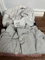 Three folded men's dress shirts stacked on floor; checkered and plaid patterns visible.