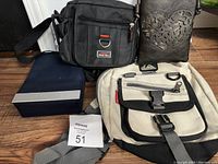 Four bags displayed on floor including black crossbody, blue Azzaro shoulder bag, small black handbag with heart design, beige and black canvas messenger bag