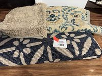 Three carpets stacked: beige shaggy texture on top left, beige with blue floral design top right, dark blue with beige leaf pattern bottom.