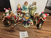 Photo showing assortment of Christmas figurines including carolers, musicians, snowman, a pumpkin-headed figure, and a miniature train set arranged on the floor.