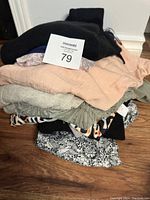 Stacked pile of assorted ladies shirts and sweaters in various colors and prints, placed on wooden floor.