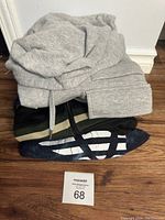 Photo of three folded men's hoodies and sweaters stacked on each other showing texture, color, and partial design.