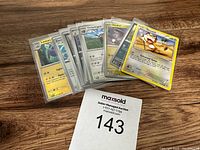 Photo of nine Pokemon trading cards laid out fanned on a wooden surface, each card in clear protective sleeves, featuring characters like Lanturn, Electrike, Oinkologne, Noibat and Meowth.
