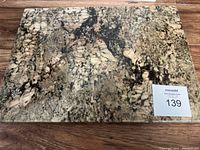 Top view of rectangular marble cutting board showing natural stone pattern and care label with auction number 139