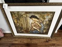 Frontal photo of the framed painting showing the female figure holding a child with an ornately carved frame and light matting.