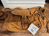 Front and top view of brown genuine leather Roots handbag showing flap with buckle closure, multiple exterior compartments, and adjustable strap.