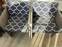 Two gray wicker outdoor arm chairs side-by-side with gray and white patterned cushions on seat and back.