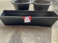 Two round black plastic planters and one long rectangular black plastic planter placed on concrete floor.